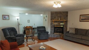 Una sala de estar con chimenea de piedra, dos sillones, un sofá y una mesa de centro de madera.