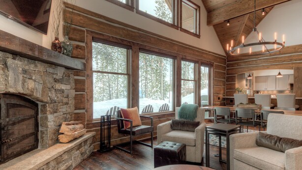 A log cabin interior with a stone fireplace, wooden floors, and large windows offering a view of the forest. -   Luxury Home, Ideal Winter Ski-in/Ski-out or Summer Basecamp (Big Sky)