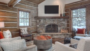A log cabin interior with a stone fireplace, leather furniture, and large windows. -   Luxury Home, Ideal Winter Ski-in/Ski-out or Summer Basecamp (Big Sky)