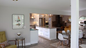 Eine moderne Küche mit weißen Schränken, einem Edelstahlkühlschrank und einem Essbereich mit weißen Stühlen und einem Glastisch.