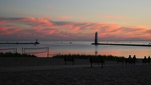 Une plage avec un phare, une mer calme et une clôture agrémentée de bancs.