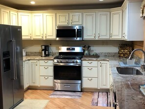 A modern kitchen with white cabinets, stainless steel appliances, and a granite countertop. - Secluded Luxury Log Cabin on 40 Acres Near Tygart River & Lake (Moatsville)