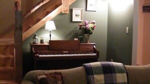 A cozy living room with a wooden staircase, a piano, and a couch with a plaid blanket.