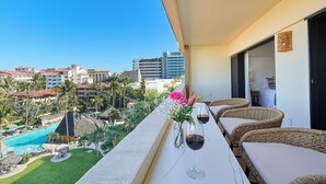 A balcony with wicker furniture, a pool, and a view of a resort area. - Beautiful condo located one block to Medano beach and The Cabo Marina (Cabo San Lucas)