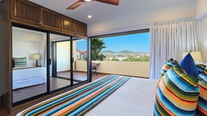 A bedroom with a large bed, a view of the city, and a balcony with a table and chair. - Beautiful condo located one block to Medano beach and The Cabo Marina (Cabo San Lucas)
