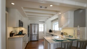 Cocina moderna con armarios blancos, electrodomésticos de acero inoxidable y una isla central con asientos tipo barra.