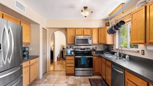 A modern kitchen with stainless steel appliances, wooden cabinets, and a large window providing natural light. - Beautiful Santa Fe Oasis. Golf, hiking & biking paradise, 20 min drive to UofA. (Tucson)