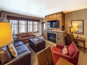 A living room with a stone fireplace, a television mounted above it, a sofa, a red armchair, and a coffee table.