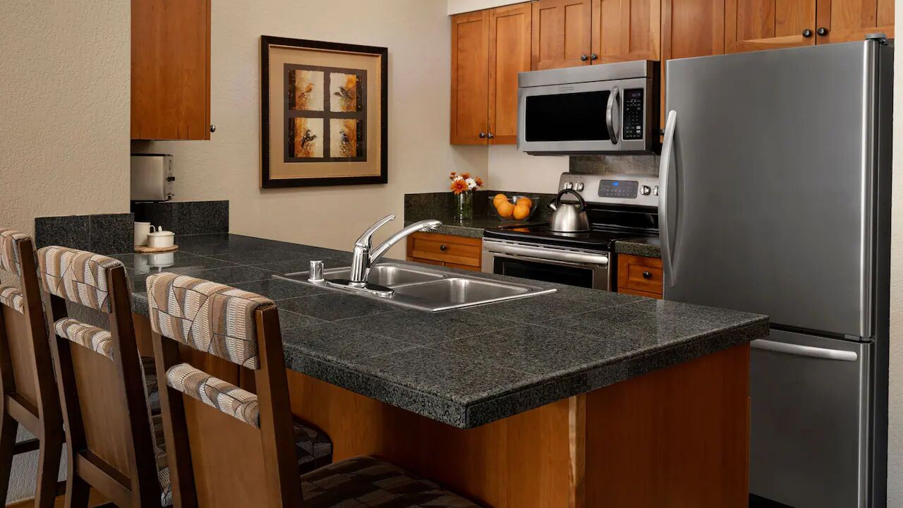 A kitchen with granite countertops, wooden cabinets, a stainless steel refrigerator, a microwave, and a stove.
