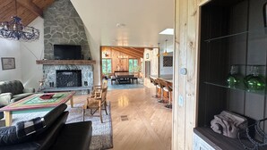 Un vaste espace de vie agrémenté d’une cheminée en pierre, d’un plafond en bois et d’un coin repas avec des tabourets de bar.