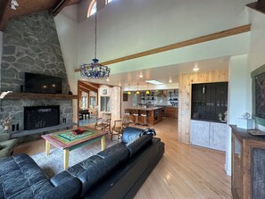 A spacious living area with a stone fireplace, a large black leather sofa, and a wooden dining table.