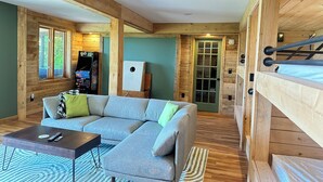 Une pièce confortable avec un canapé d’angle, une table basse, une console de jeux et un lit superposé.