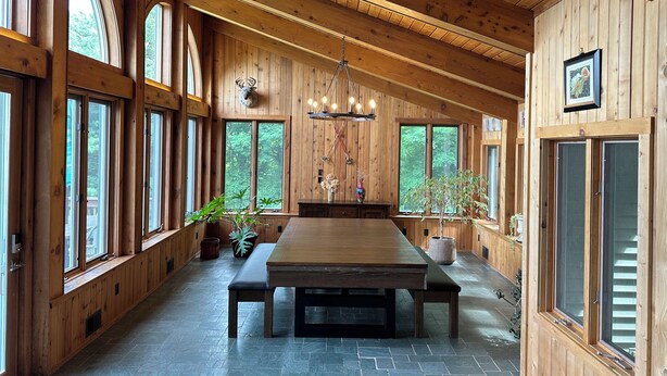 Un intérieur spacieux en bois, doté de grandes fenêtres, d’une grande table à manger et d’un lustre.