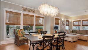 Uma área de refeições com uma mesa, cadeiras e um candelabro. Há uma placa acima das janelas com a inscrição "BEACH HOUSE".