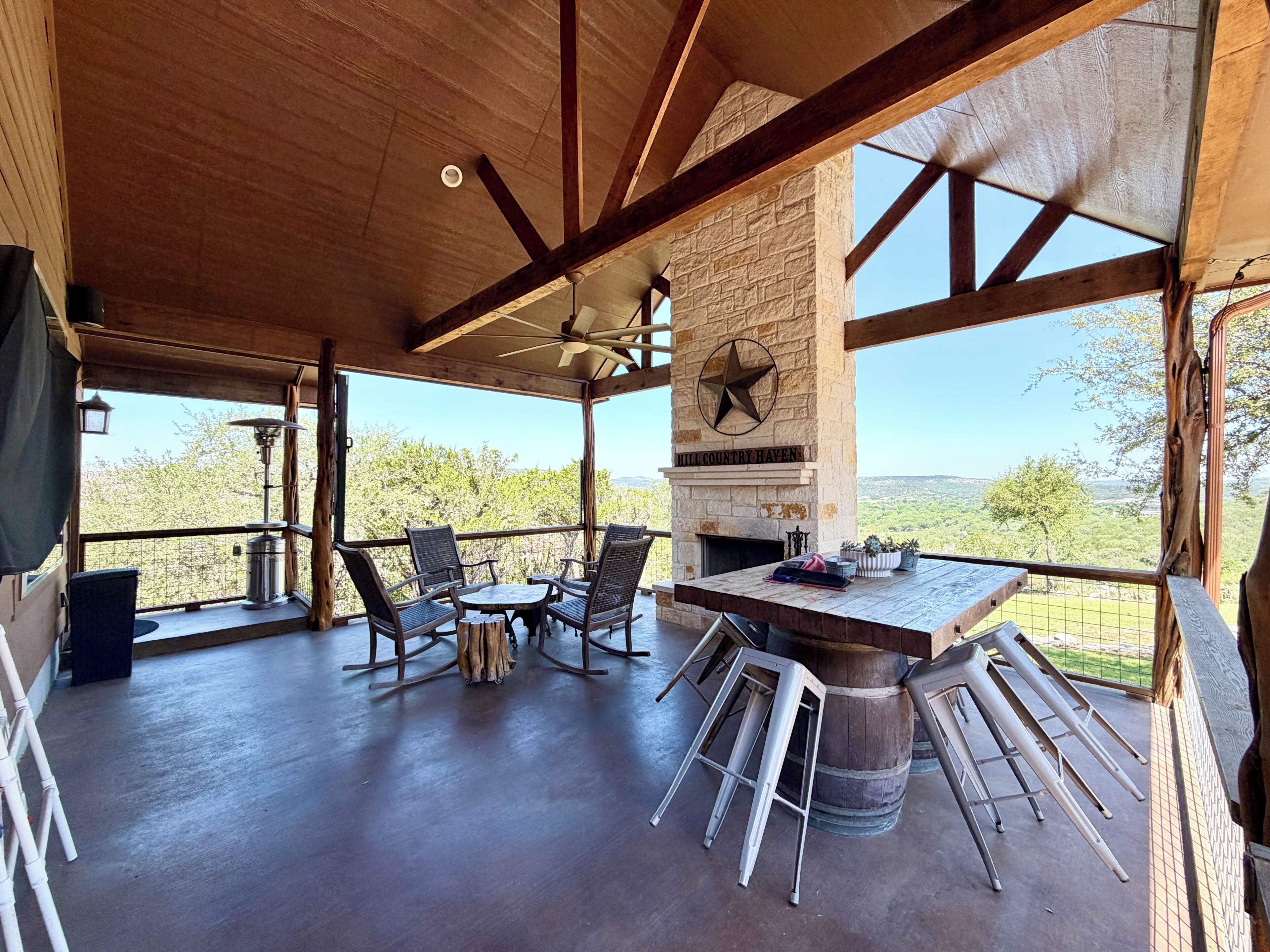 A spacious patio with a stone fireplace, wooden beams, and a view of the landscape.
