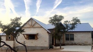 A two-story stone house with a metal roof, a dirt driveway, and a small tree in the foreground. - Guadalupe River, Whitewater Amphitheater, New Braunfels, Canyon Lake, Gruene (New Braunfels)