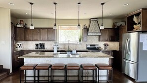 A modern kitchen with a large island, bar stools, stainless steel appliances, and pendant lighting. - Guadalupe River, Whitewater Amphitheater, New Braunfels, Canyon Lake, Gruene (New Braunfels)