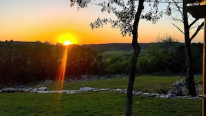 A sunset over a grassy field with a tree in the foreground and a stone border. - Guadalupe River, Whitewater Amphitheater, New Braunfels, Canyon Lake, Gruene (New Braunfels)