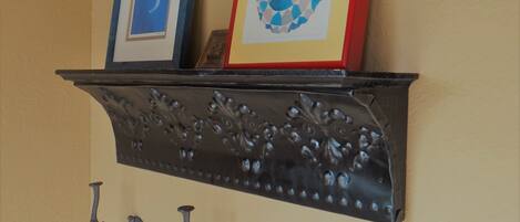 A black metal shelf with two framed artworks and three wall-mounted hooks.