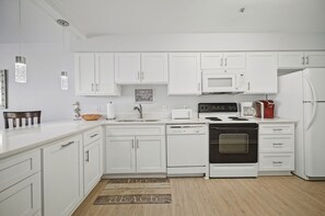 Una cocina moderna con armarios blancos, horno empotrado, microondas y cafetera.