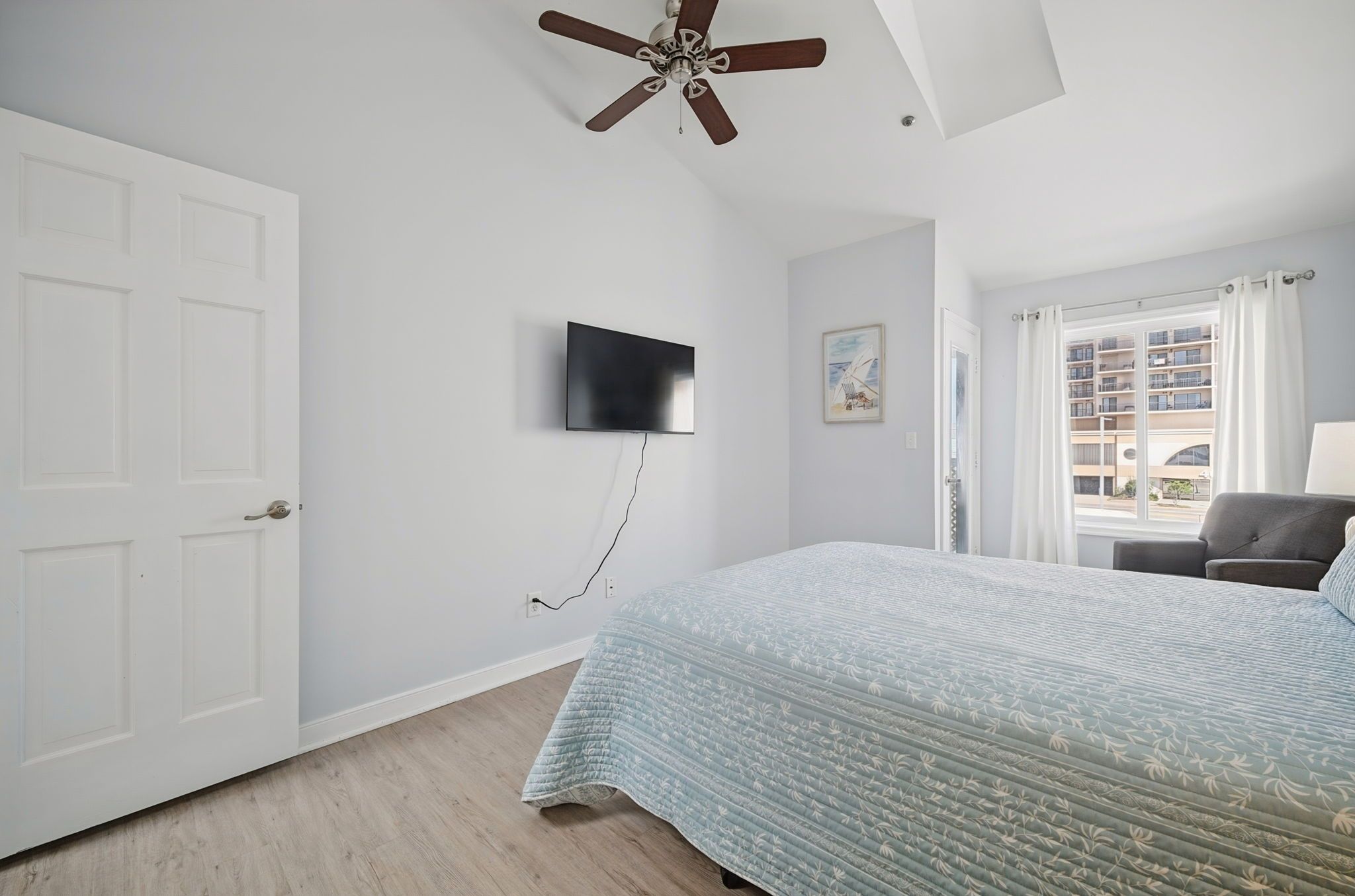 A bedroom with a bed, a ceiling fan, a mounted TV, and a window with curtains.