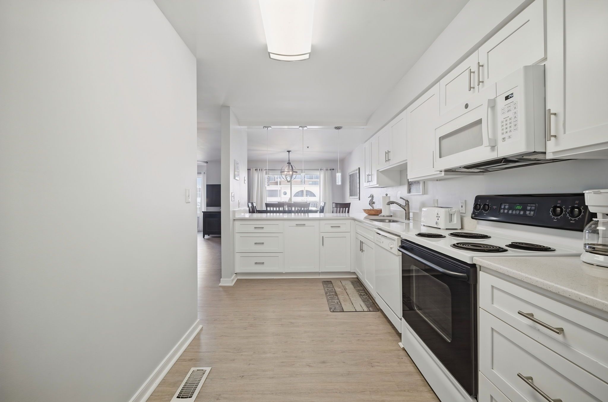 A modern kitchen with white cabinetry, a black stove, and a dining area with a view.