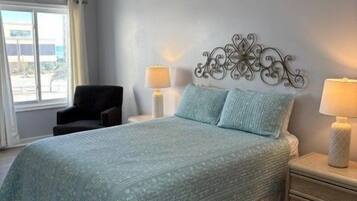A bedroom with a bed, bedside lamps, a chair, and a window.