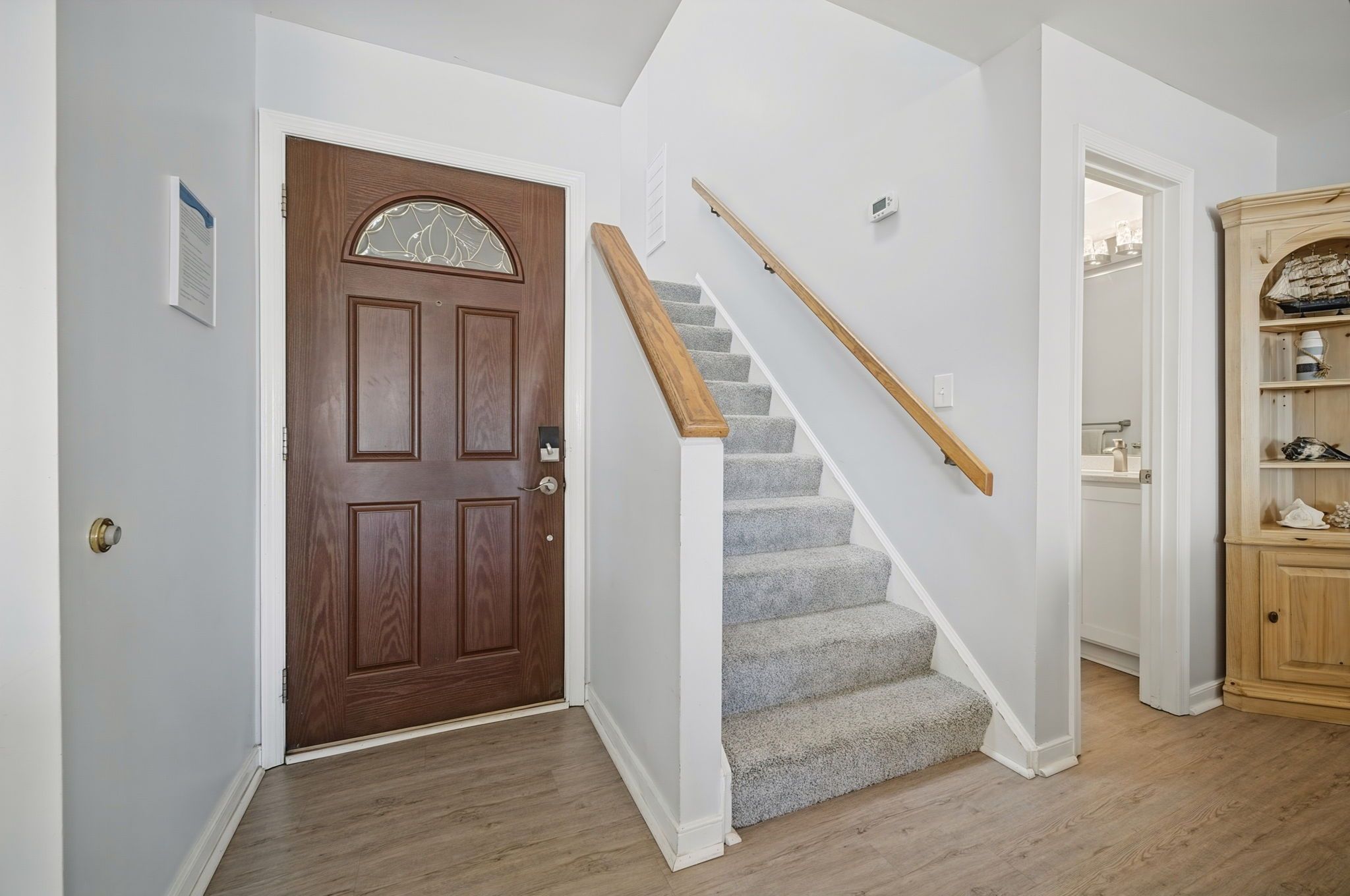 A staircase with a wooden handrail leading to a landing, a wooden door with a decorative glass panel, and a wooden cabinet with decorative items.
