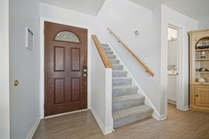 A staircase with a wooden handrail leading to a landing, a wooden door with a decorative glass panel, and a wooden cabinet with decorative items.