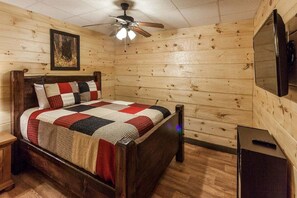 A wooden-paneled room with a bed, a ceiling fan, a TV, and a small table.