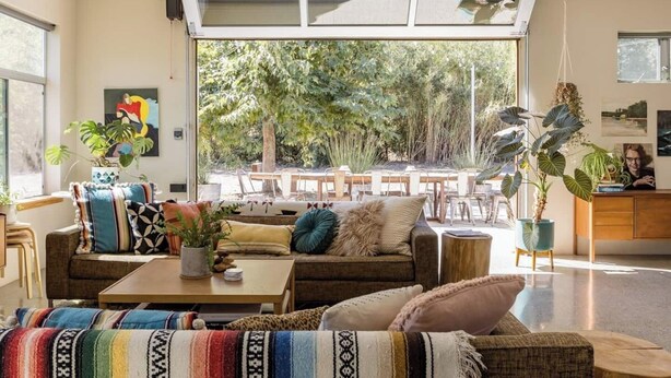 Un amplio espacio de sala con un ventanal grande, un sofá, una mesa de centro y un comedor a la vista a través del ventanal.