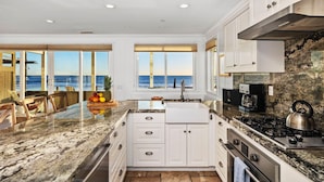 A kitchen with white cabinets, a granite countertop, a stainless steel stove, and a view of the ocean. - OCEANFRONT CHIC LUXURY HOME (Capistrano Beach)