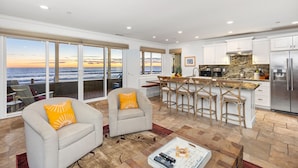 A spacious living area with a large window overlooking the ocean, a kitchen with a stone backsplash, and a bar area with stools. - OCEANFRONT CHIC LUXURY HOME (Capistrano Beach)