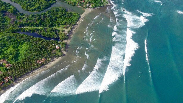 Luchtbeeld van een kustgebied met weelderige begroeiing, een rivier en een strand.