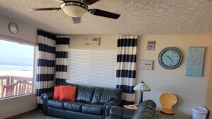 Un salón con un sofá de cuero negro, una silla de madera, un reloj y una ventana con cortinas a rayas.