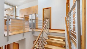 A modern interior with a wooden staircase, metal railings, and a kitchen area with wooden cabinets and a refrigerator. - Best spot in town! Modern townhome, downtown Hood River, big views! (Hood River)