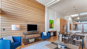 A modern living room with a flat-screen TV, blue sofas, a wooden coffee table, and a kitchen area with wooden cabinets and a dining table. - Best spot in town! Modern townhome, downtown Hood River, big views! (Hood River)