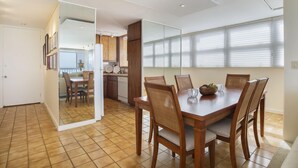 A modern kitchen with wooden cabinets, a dining table with chairs, and a large window with blinds.