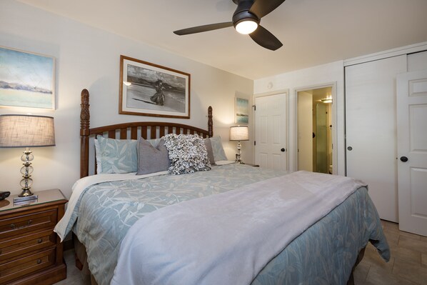 A bedroom with a bed, nightstands, a ceiling fan, and a door.