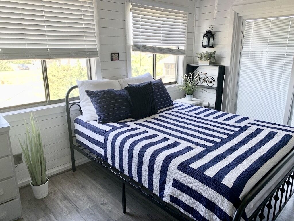 A bed with a striped bedspread, a potted plant, and a nightstand with a lamp and decorative items.