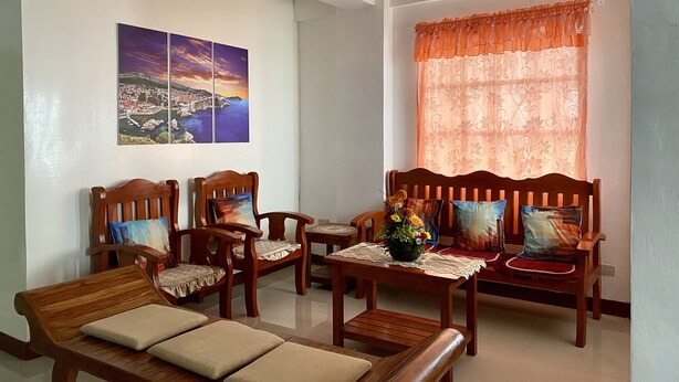 A living room with wooden furniture, a painting of a coastal landscape, and a window with a floral curtain.