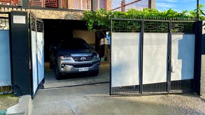 A car parked in a garage with a gated entrance, a building with red window grills, and a clear sky.