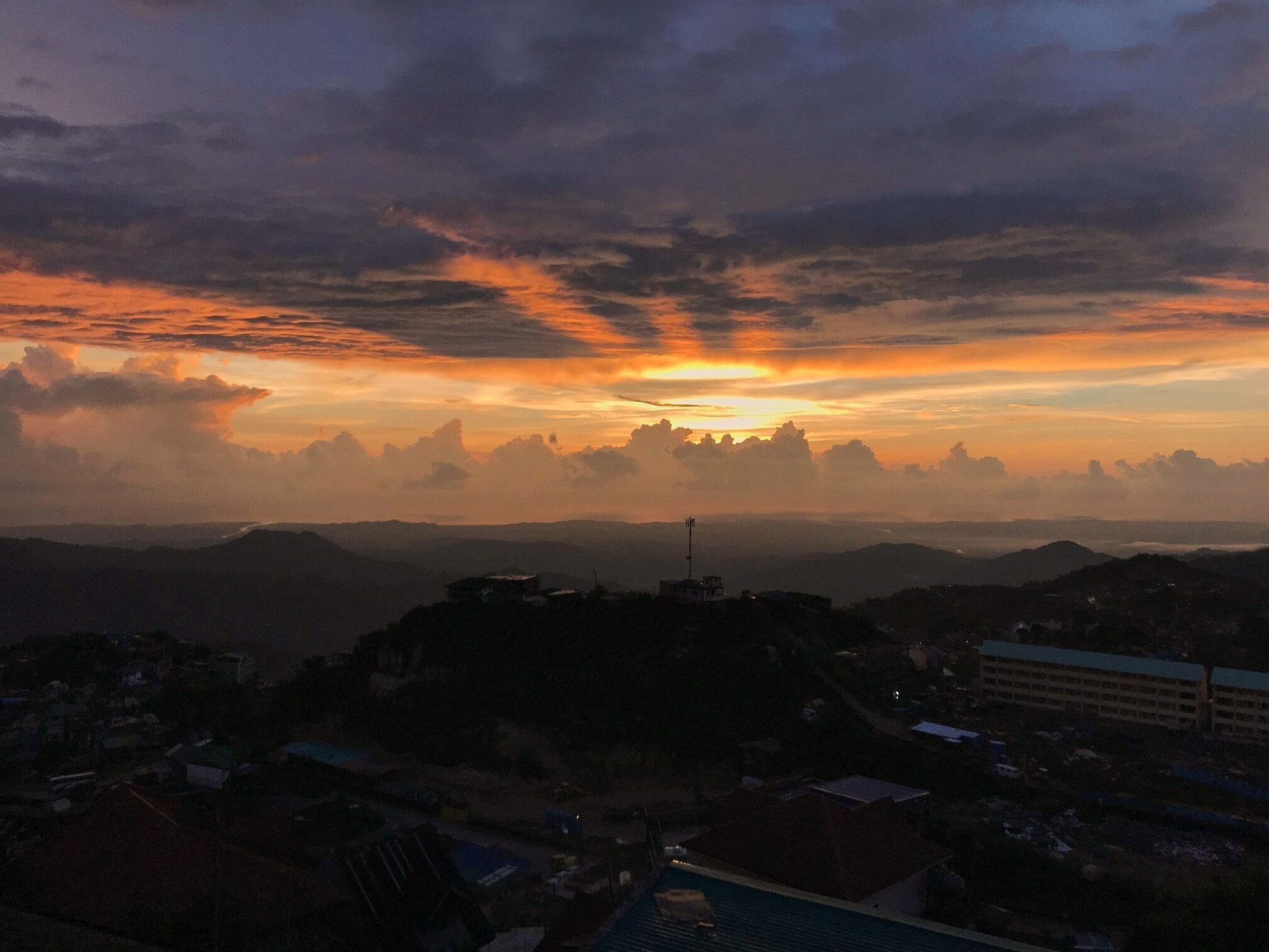 A sunset over a mountainous landscape with buildings in the foreground.