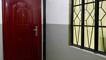 Una puerta roja con un tirador de metal, una ventana con diseño geométrico y un piso de baldosas con felpudo.