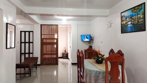 A dining area with a table set for four, a TV mounted on the wall, and a painting above the table.