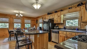A cabin-style kitchen with wooden walls, a central island, bar stools, a refrigerator, stove, and a sink. - Summers' Ridge by Mountain Oasis | Dog-Friendly Cabin in Coosawattee River Resort (Ellijay)