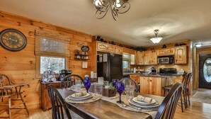 A wooden interior with a dining table set for four, a kitchen with wooden cabinets, a refrigerator, and a microwave. - Summers' Ridge by Mountain Oasis | Dog-Friendly Cabin in Coosawattee River Resort (Ellijay)