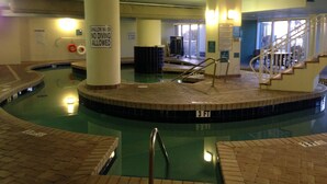 Una piscina interior con un pilar central, un cartel de advertencia sobre poca profundidad y un indicador de profundidad de 3 pies.