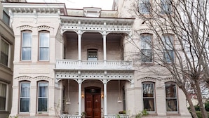 Un edificio histórico con una entrada central, un porche de dos pisos y múltiples ventanas.