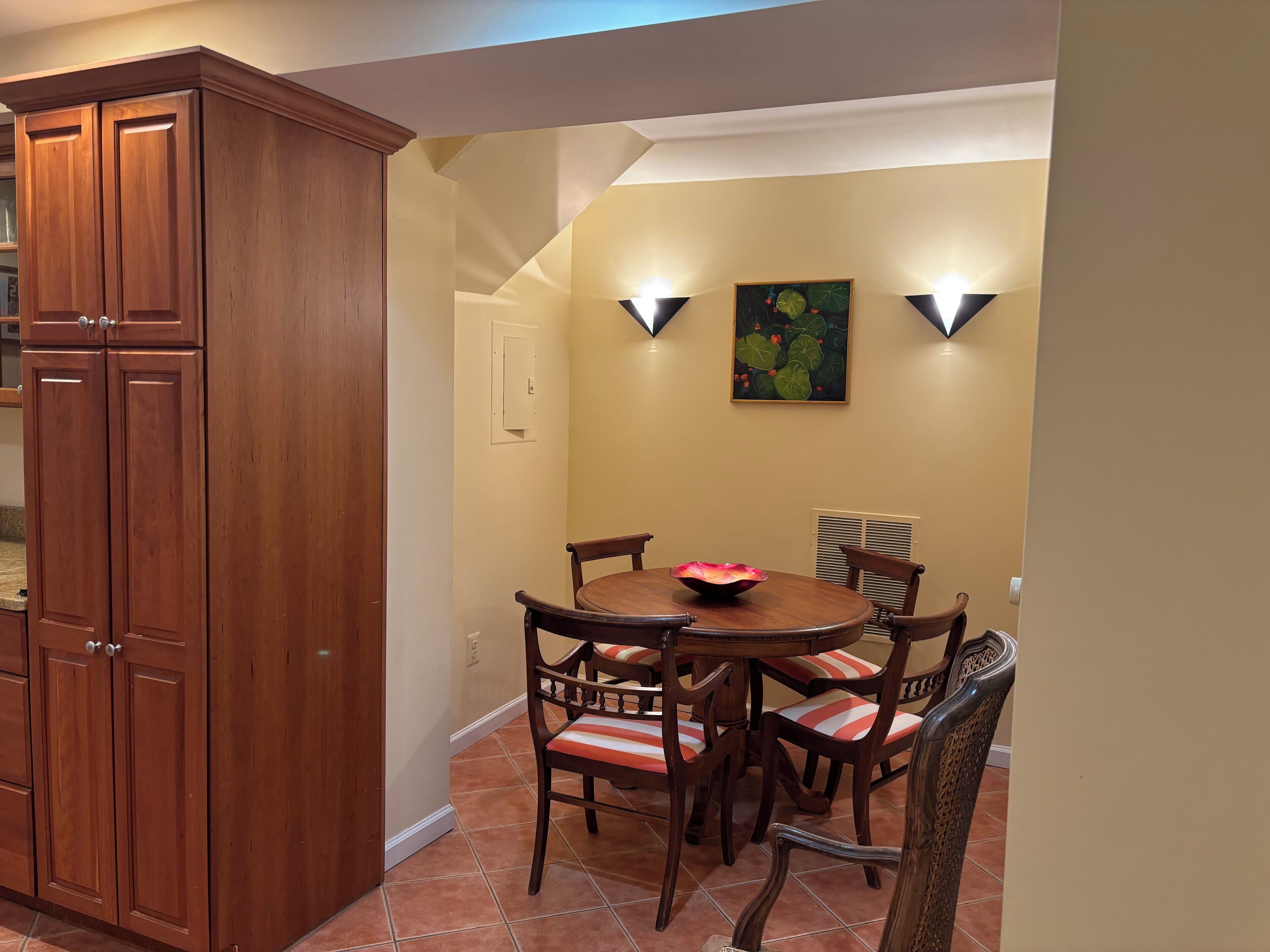 Un comedor con un armario de madera, una mesa redonda y sillas con cojines a rayas.